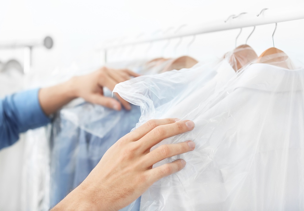 Hands sorting clothes covered in plastic garment bags on hangers, hanging on a clothing rack.