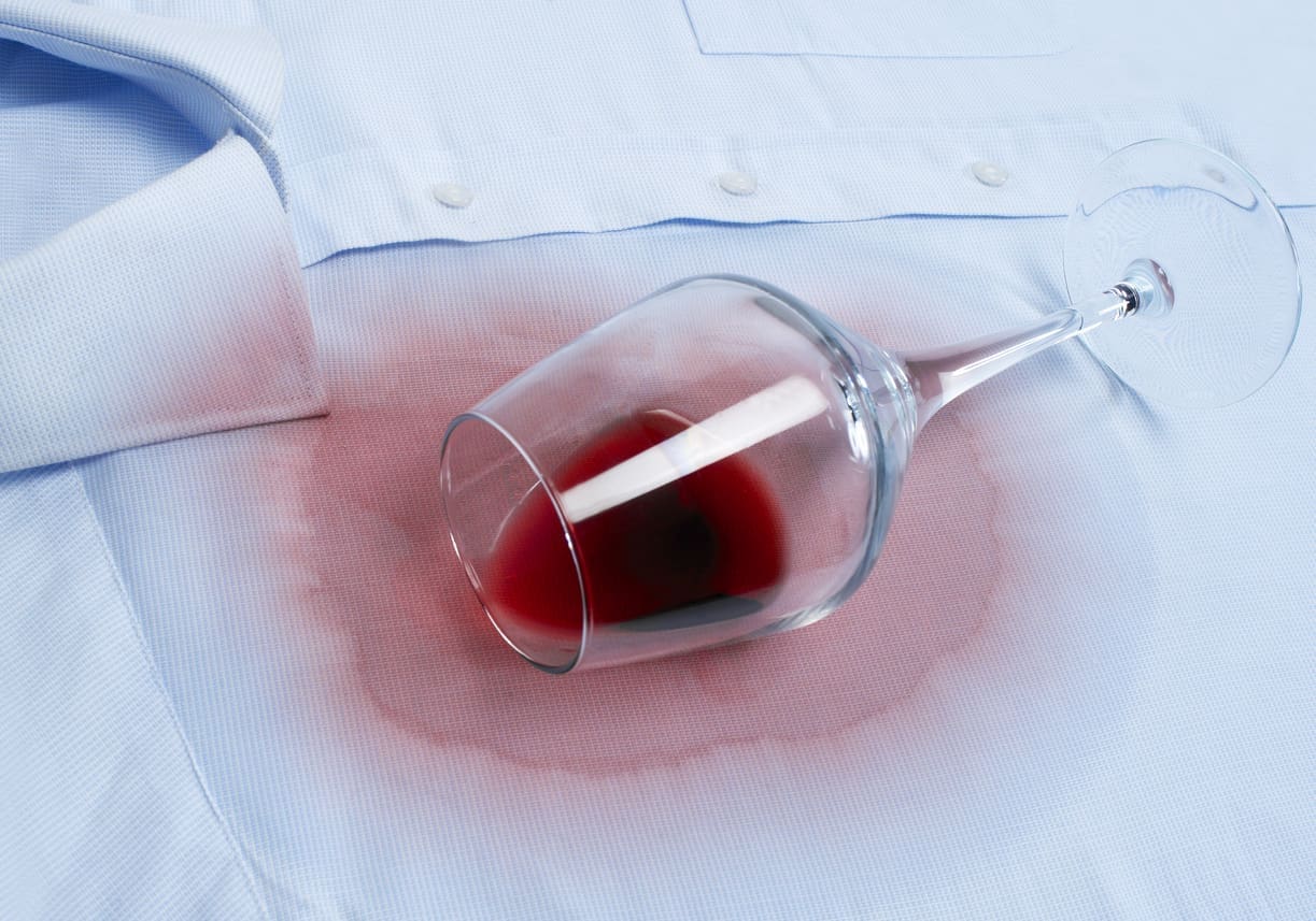 A glass of red wine tipped over on a light blue shirt, leaving a large wine stain around the glass&mdash;prompting the need for tips on how to remove red wine stains from suits or finding reliable dry cleaning near me Myrtle Beach South Carolina.